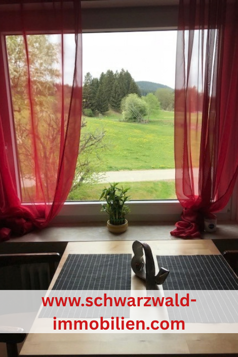 Ein Tisch vor einem Fenster mit Blumen darauf, ein roter Vorhang und Blick auf die Wiese